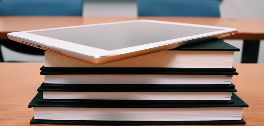 Auf einem Stapel Bücher, deren Rücken zu sehen ist, liegt ein Tablet.