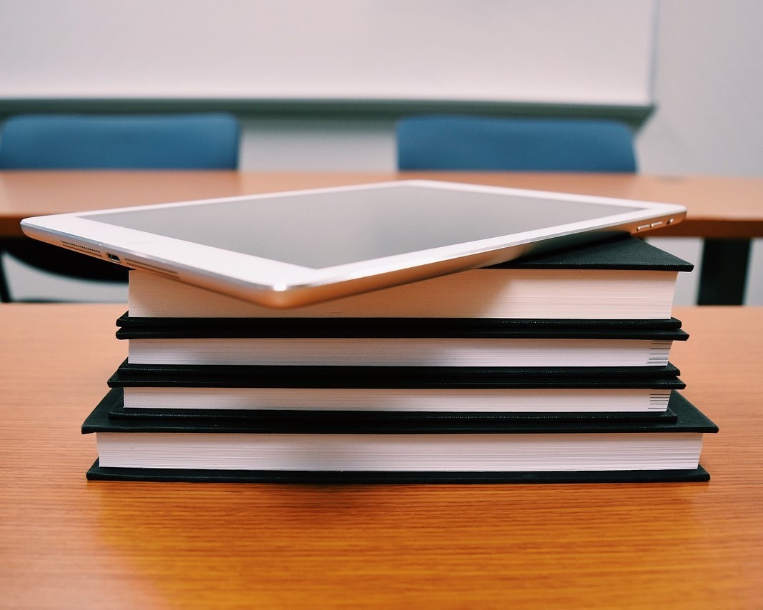 Schulbuch- und Tabletausleihe Auf einem Stapel Bücher, deren Rücken zu sehen ist, liegt ein Tablet.