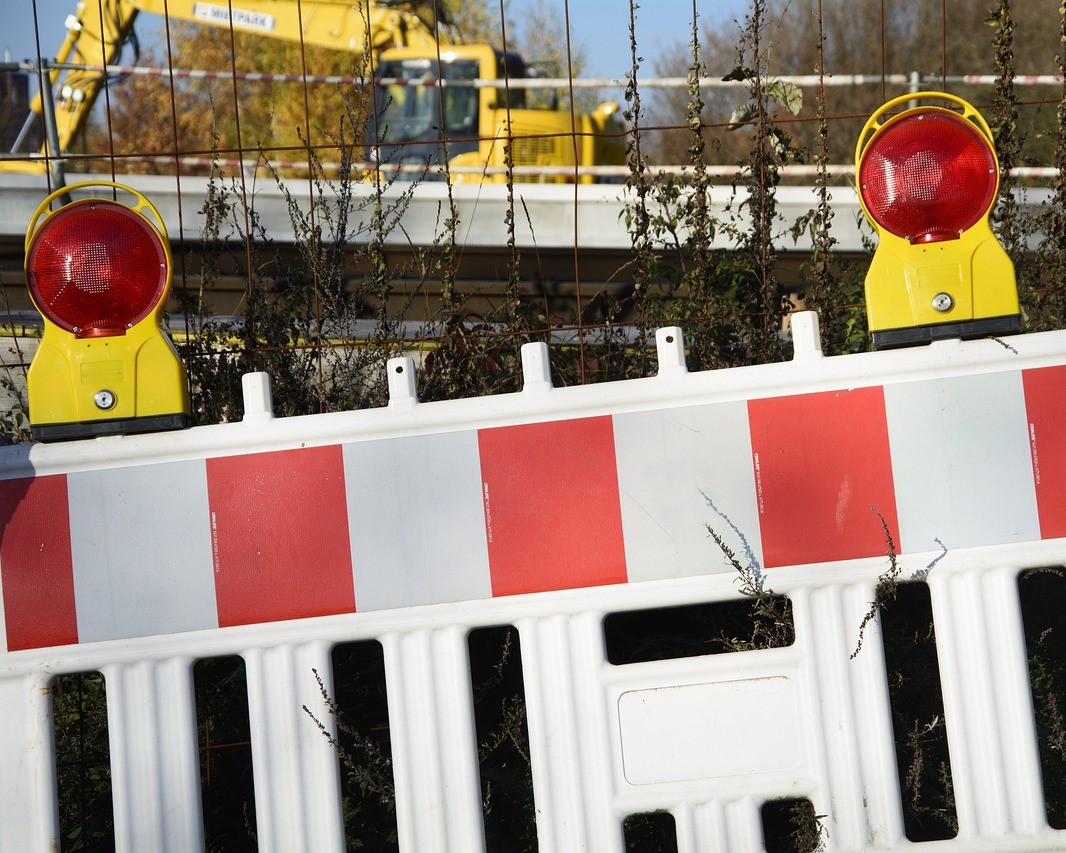 Teil einer Straßensperrung vor einem Zahn in Großaufnahme. im Hintergrund ist ein Bagger zu erkennen., der auf einer Straße im Einsatz ist. 
