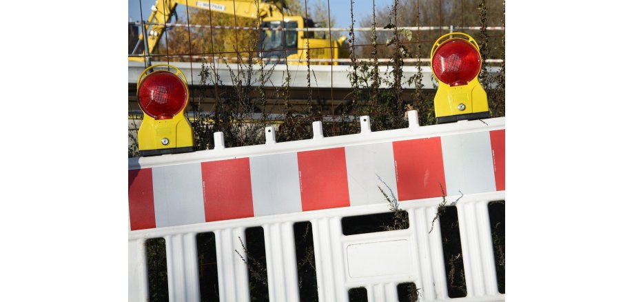 Teil einer Straßensperrung vor einem Zahn in Großaufnahme. im Hintergrund ist ein Bagger zu erkennen., der auf einer Straße im Einsatz ist.
