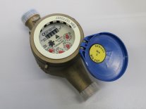 Ein Wasserzähler mit geöffneter, blauer Klappe liegt auf einem grauen Untergrund. 