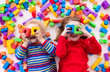 Zwei Kinder spielen mit den bunten Bausteinen  sie halten sie sich vor ihr Gesicht und formen eine Brille.
