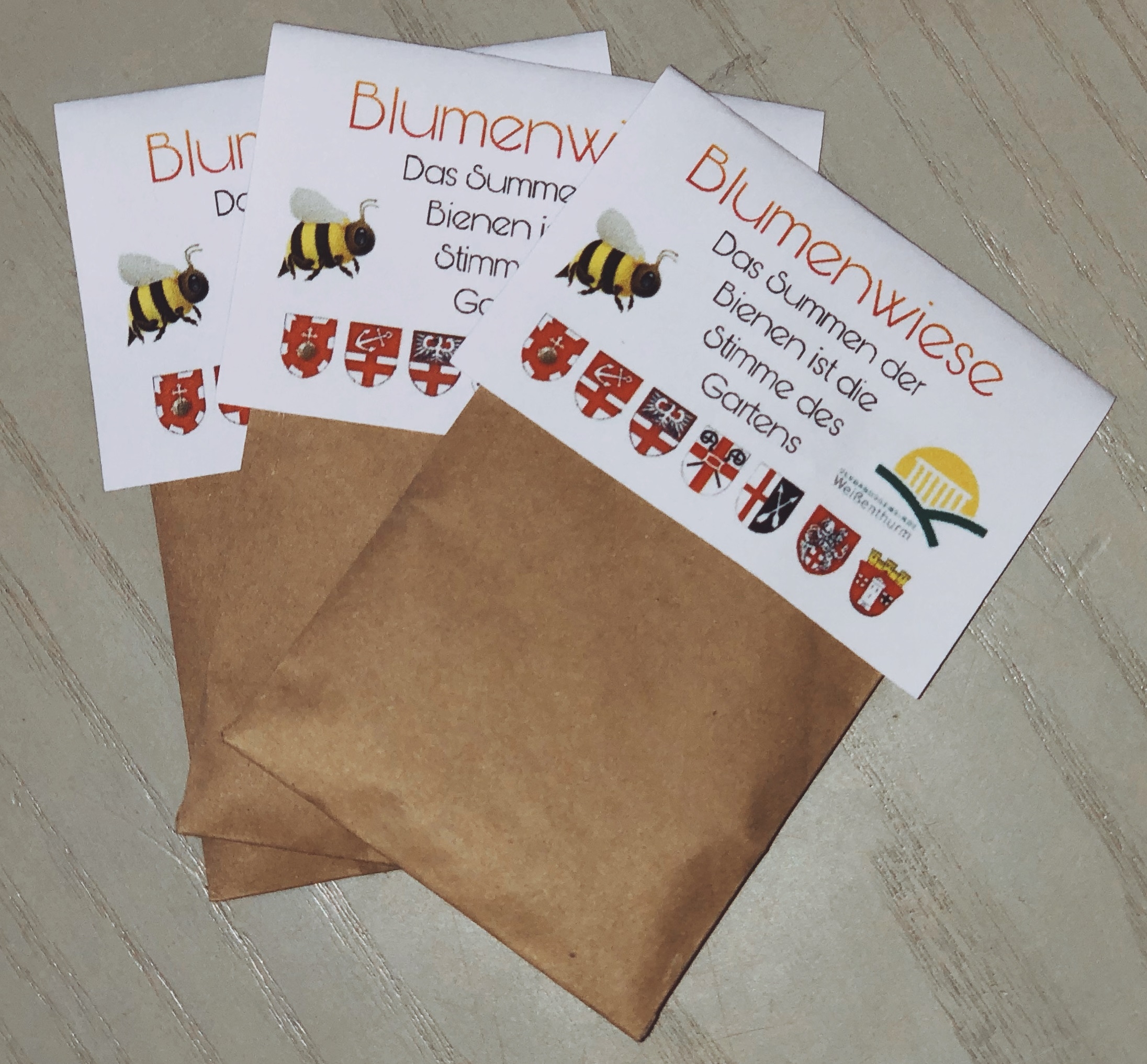 Drei braune Tütchen mit Blumensamen liegen auf dem Tisch.