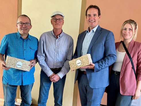 Besuch bei NICK Naturbaustoffe VG-Bürgermeister Thomas Przybylla, Wirtschaftsförderin Kim Lachmann und der Weißenthurmer Stadtbürgeremister Johannes Juchem zeigen mit Joachim Schlauß von NICK Naturbaustoffe den Hanfkalkstein Canabloc.
